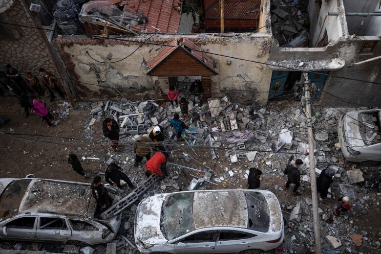 People assess the damage in a street strewn with rubble and destroyed vehicles.