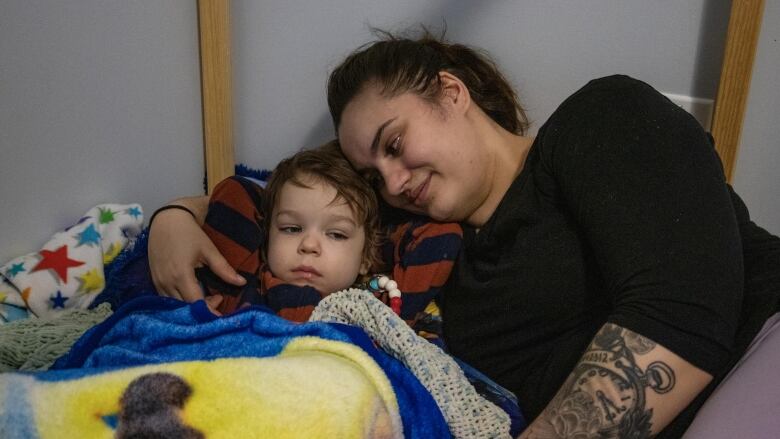 A woman and boy cuddle in bed.