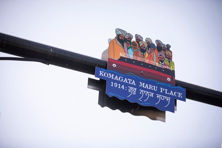 A sign depicting a dozen South Asian people looking sad sits on a pole, with the words 'Komagata Maru Place'.