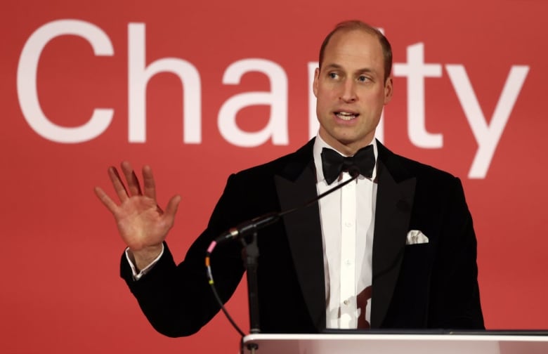 A person speaks at a podium behind a microphone and in front of a wall with the word Charity on it.