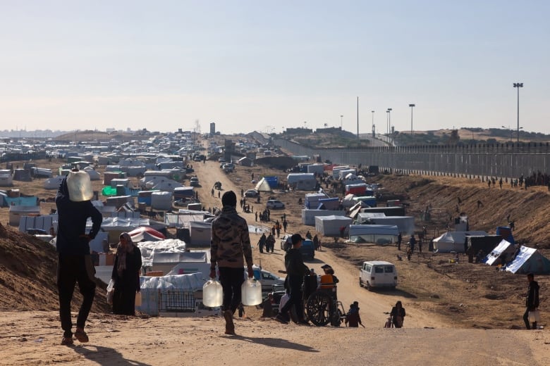 People carrying water walk toward a makeshift camp site.