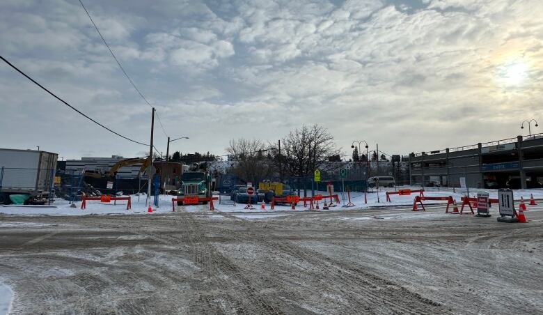 a snowy street is blocked off by orange construction signs and trucks.