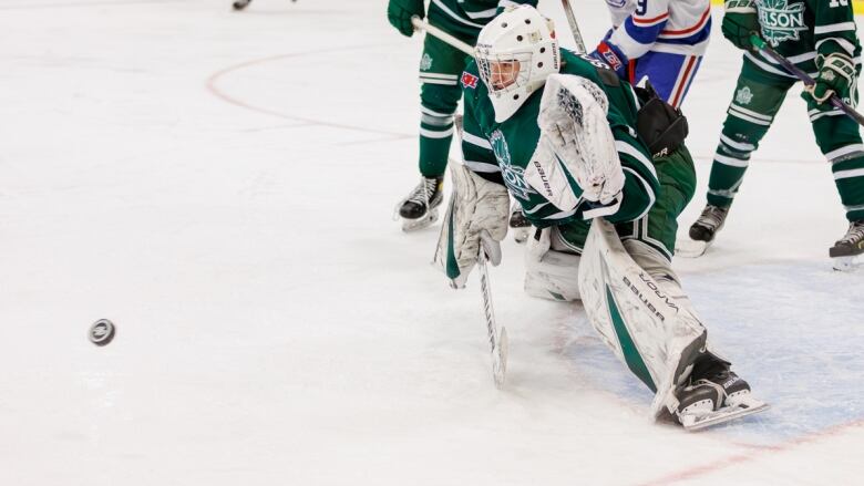 A hockey goaltender looks to save a puck on the ice, as other skaters look on.