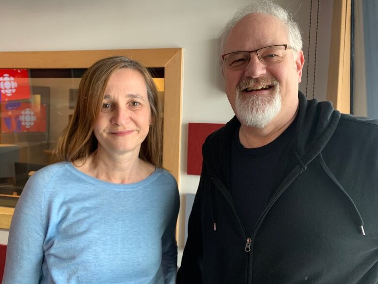 A woman with long brown hair and a man with white hair and a white beard stand next to each other, smiling.