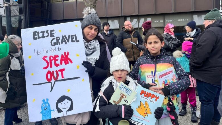 A woman and her children hold up signs and books.