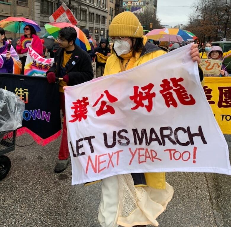 A person wearing yellow and a mask is holding a sign in Chinese and English saying 