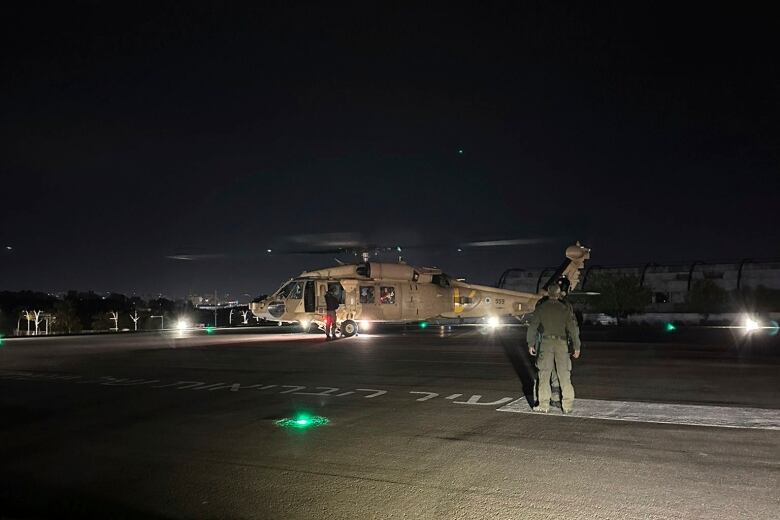 Soldiers stand near an operating helicopter parked on a tarmac.