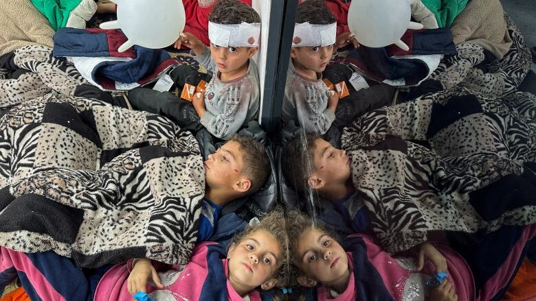 Three injured children, including one with a bandaged head, lie on the floor against a mirror as they receive treatment at a hospital, in the aftermath of an Israeli airstrike