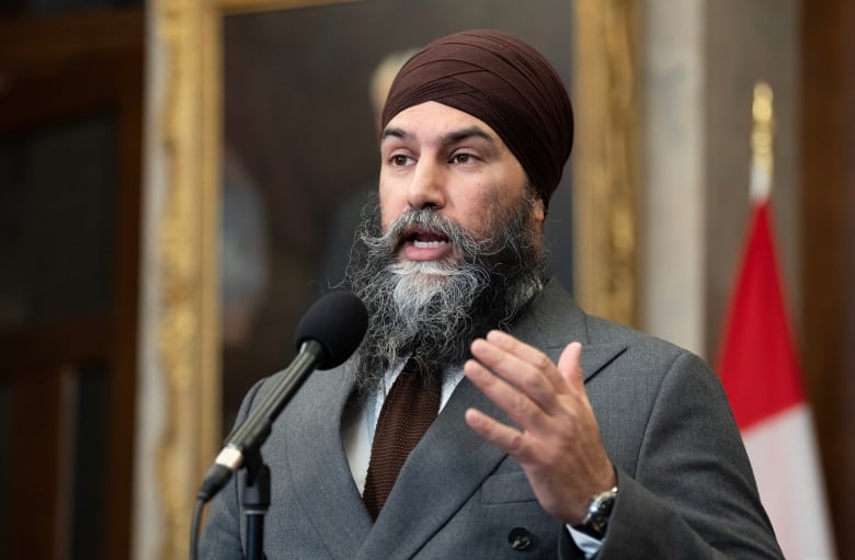 A man wearing a suit and a tie speaks at a microphone.