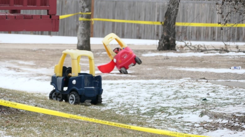 Children's toys are seen in a yard that is surrounded in yellow police tape.