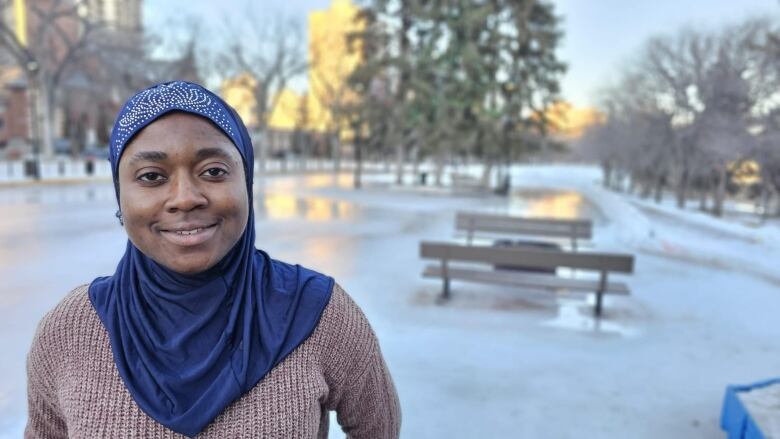 A woman in a hijab poses for a phot in front of a skating rink.