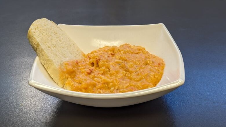 A white dish with lobster dip and a slice of baguette 