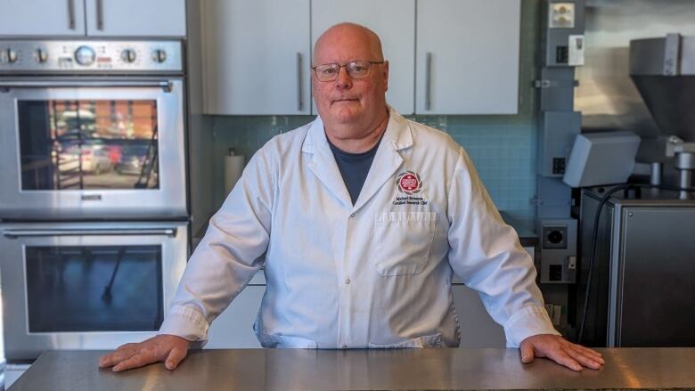 A chef in a white coat stands in a test kitchen 