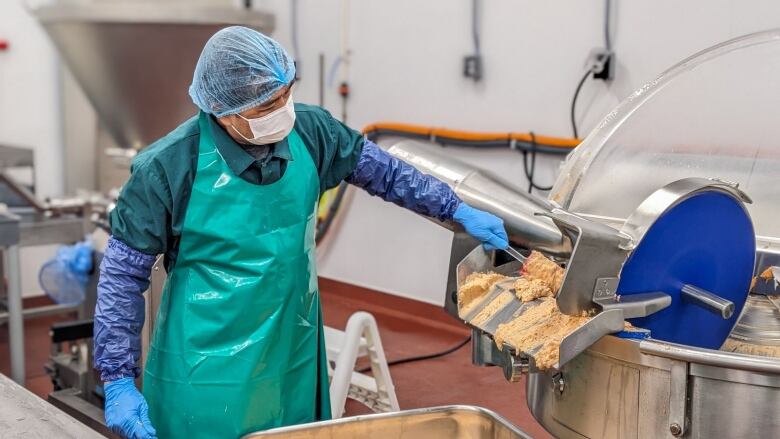 A worker in safety equipment scoops lobster dip out of a large stainless steel machine. 