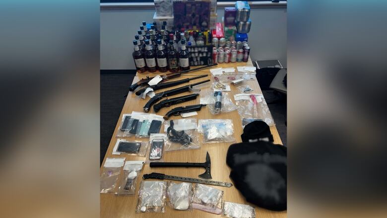 A table filled with alcohol, drugs, guns and other handheld weapons. 