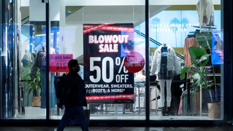 A person walks by a clothing store with a sale sign in the window.