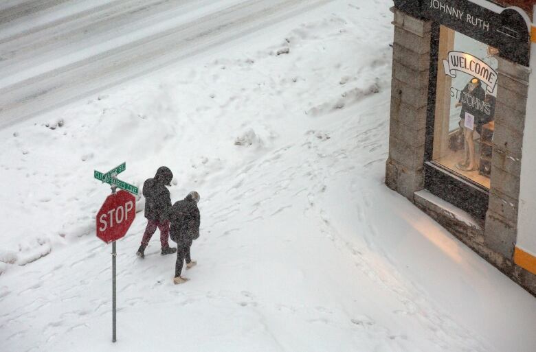 Two people walk down a sidewalk covered in snow.