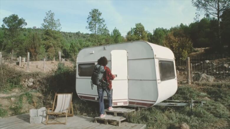 A person with a backpack on is opening the door of a tiny camper.