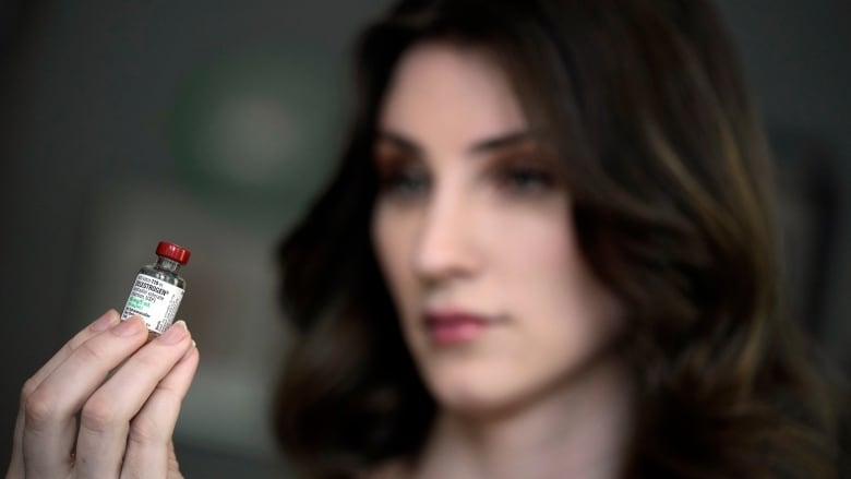 A woman holds a small vial with a medical label