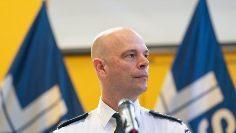 Man in white police dress shirts with insignia is flanked by blue flags with police department logo.