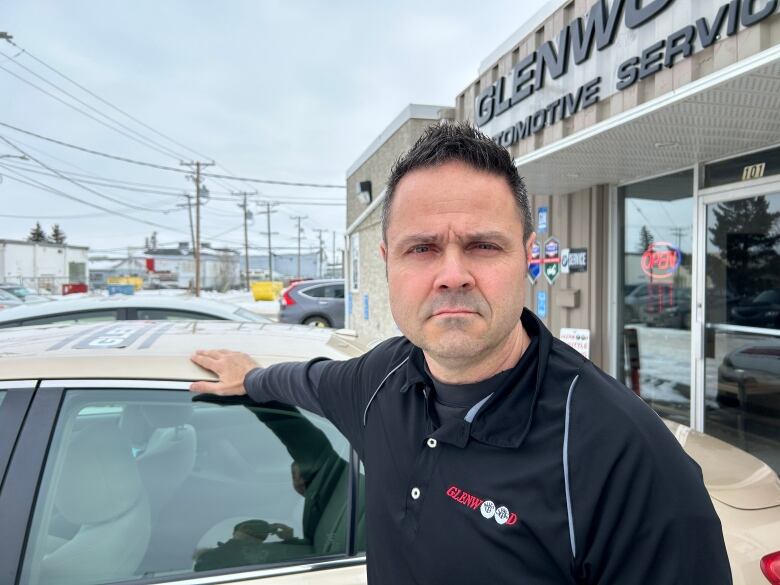 A man stands leaning against a car.