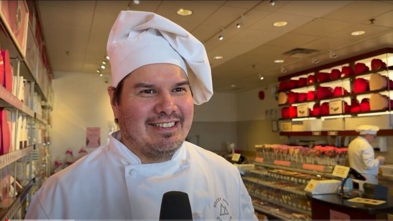 A man in chef's attire inside a chocolate shop.