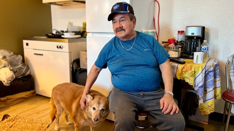 A man sits at the table petting his dog.