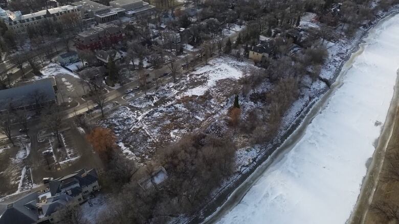 An aerial view of a snow-dusted, empty plot of land along the partly frozen Assiniboine River.