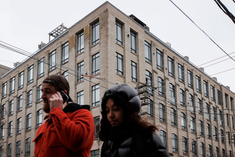 Two people wearing winter jackets walk by a large apartment complex.