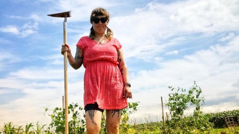 A person with pigtails holds a garden tool. A garden can be seen in the background.