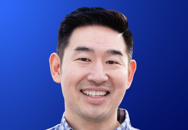 A smiling man in a checkered shirt smiles for a portrait.