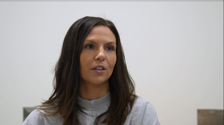 A woman with long brown hair wearing a grey mock neck shirt.