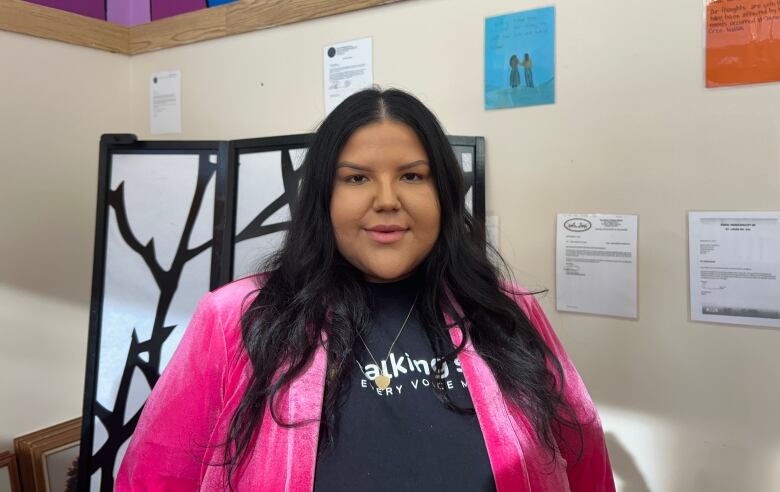 A woman poses for a photo wearing a pink blazer over a black t-shirt.