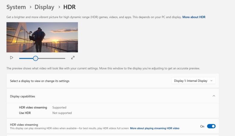A computer screen shows under System, Display, and HDR, a small video of a man walking on a ferry at sunrise. 