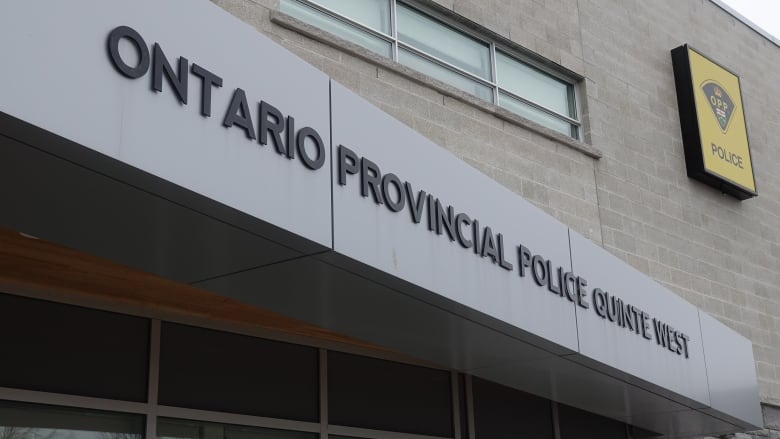 A close-up photo of a modern, brick building. A grey, metal canopy over the door says Ontario Provincial Police Quinte West. There's also a yellow sign with the OPP crest on it.