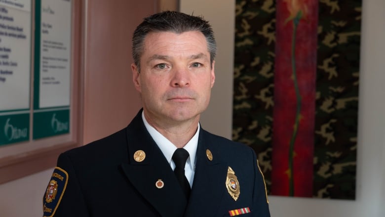 A man with short grey hair in a blue uniform stands in front of a pink wall