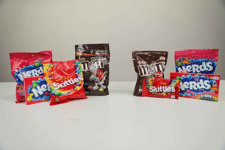 A bag of nerds, skittles, and m&m's next to european versions of the same candy. 