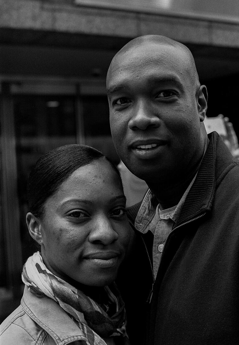 A black-and-white portrait of a Black couple, holding each other close outside.