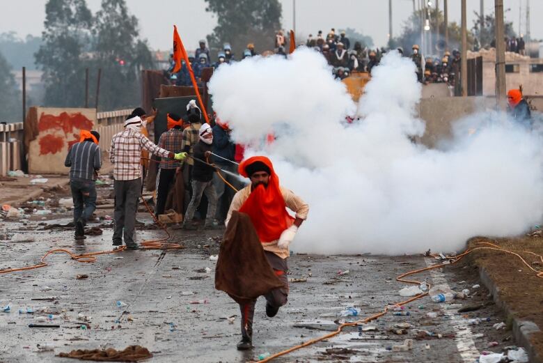 A protester runs from tear gas from police. A crowd of fellow protesters are gathered behind. 