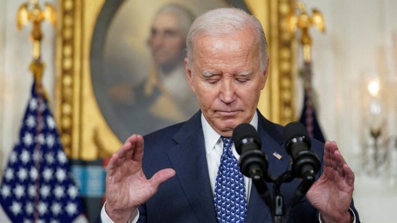 Biden looks dejected, with head down and hands up. He's standing in front of a U.S. flag and a framed portrait of George Washington.