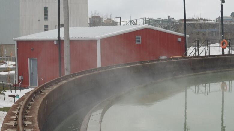 Steam rises from a greenish pool of water. Red building in background