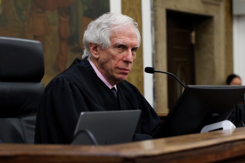 A judge is seen seated at courtroom bench.