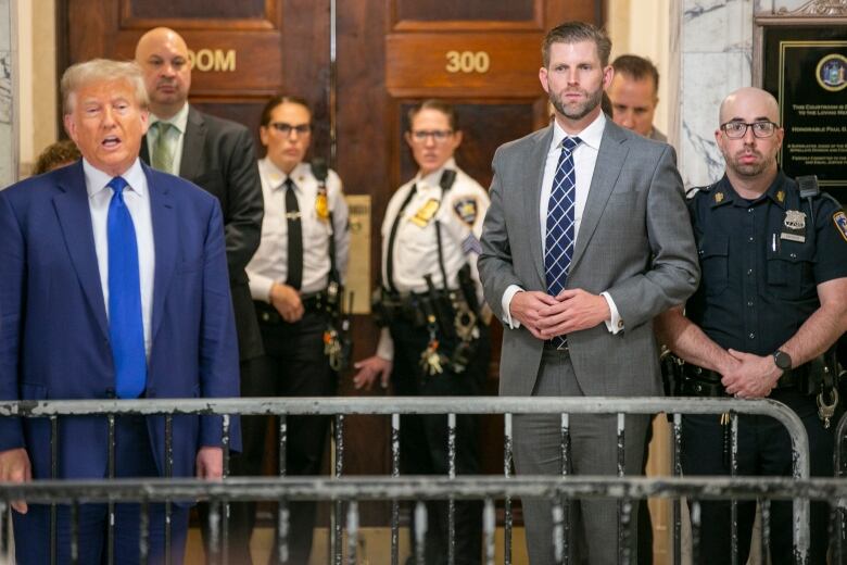 People in suits stand behind a barricade and with police officers around them.