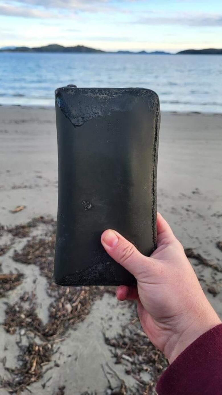 A beaten up green wallet against the backdrop of a beach and the ocean