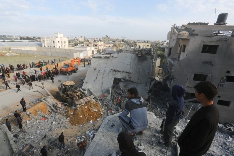 People look down at the rubble of a destroyed building.