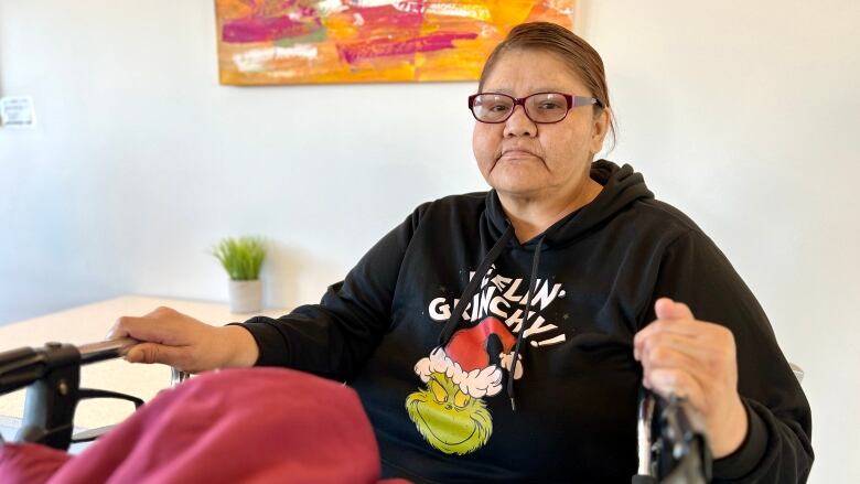 A woman sits in a chair holding the handles of her walker.