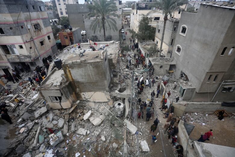 An aerial view shows people walking amid the rubble of a destroyed building.