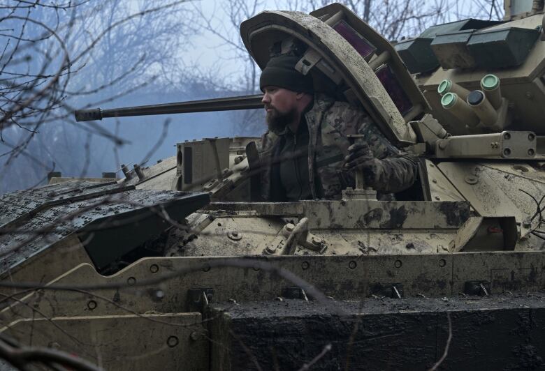 A man halfway out of a tank hatch.