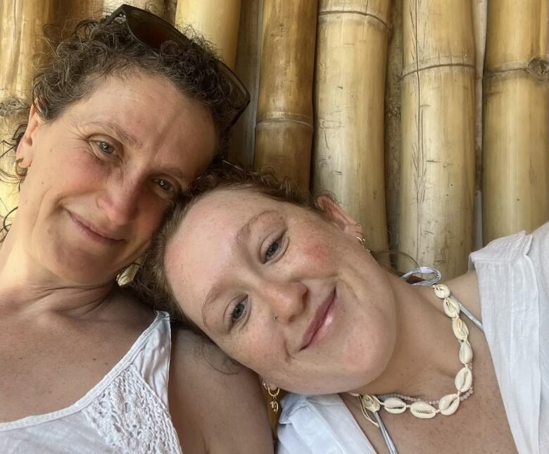 Two women in summer attire lean in toward each other and smile at the camera