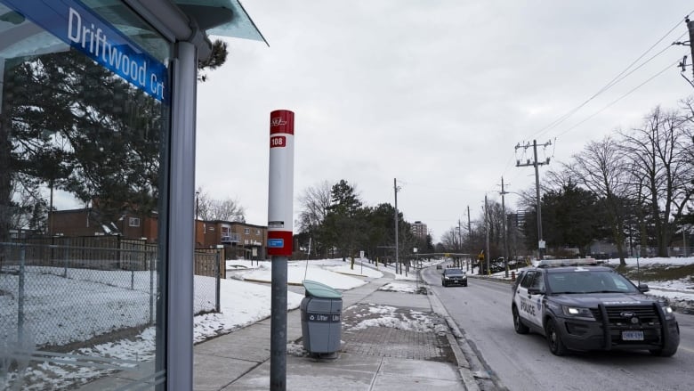 A police car is seen driving by a bus stop.